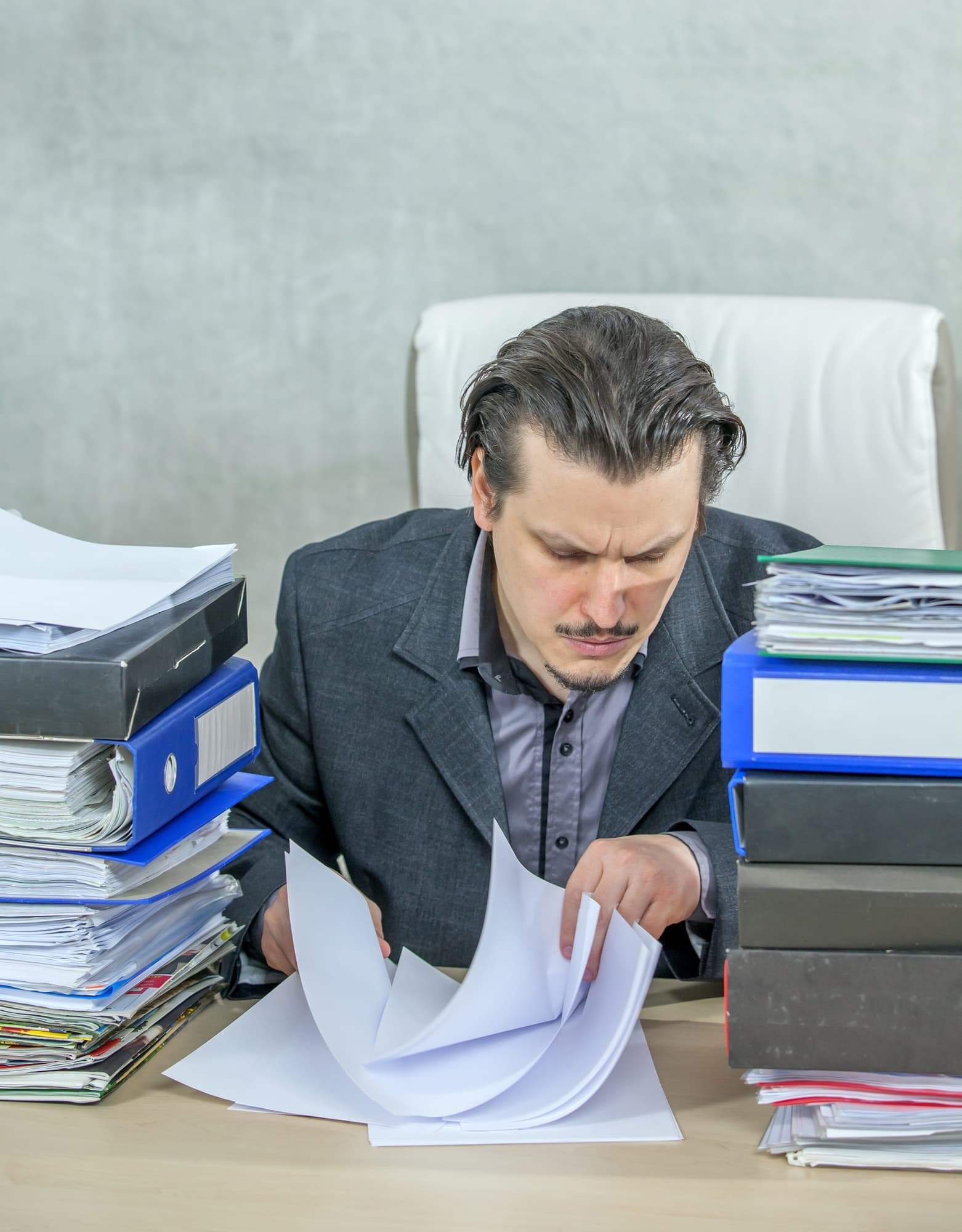 Overwhelmed professional sorting through stacks of paperwork